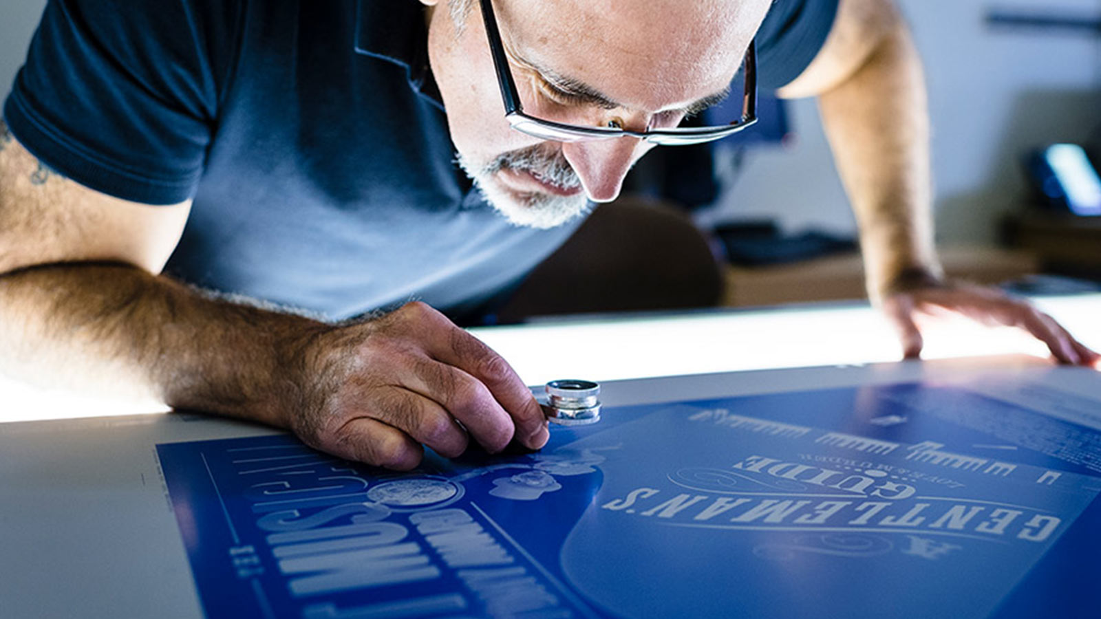 man examining print piece closely with magnifying tool